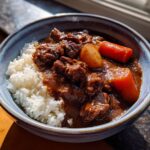 Close-up of a bowl of rich Japanese Curry Recipes with chunks of beef, carrots, and potatoes served alongside white rice.