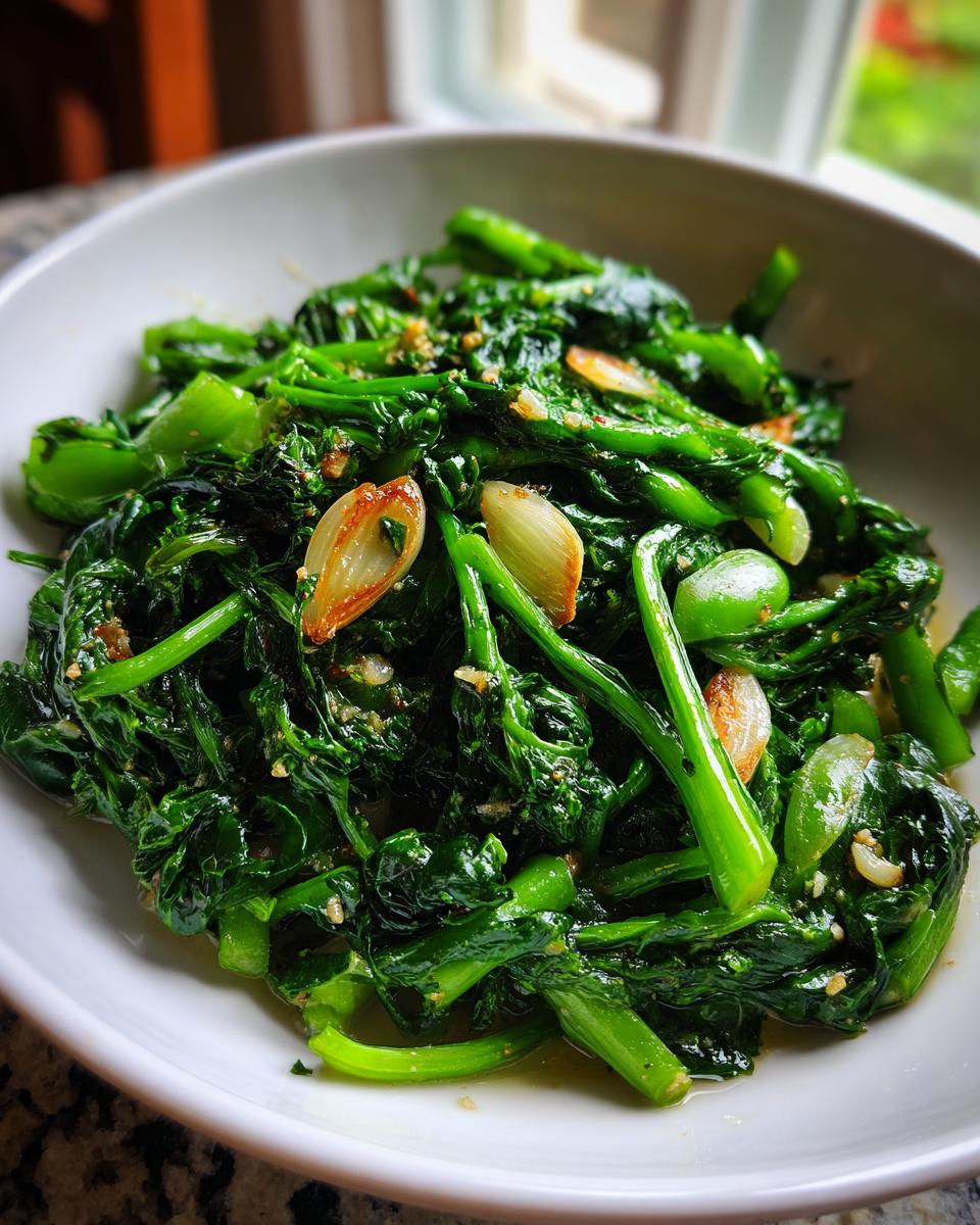 Close-up of bright green saut&eacute;ed Broccoli Rabe with large slices of toasted garlic in a white bowl.
