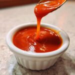 Close-up of thick, vibrant orange Catalina Dressing dripping from a spoon into a small white ramekin.