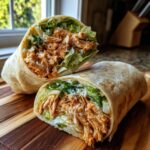 A halved Chicken Caesar Wrap showing shredded seasoned chicken, crisp lettuce, and Parmesan cheese inside a flour tortilla.