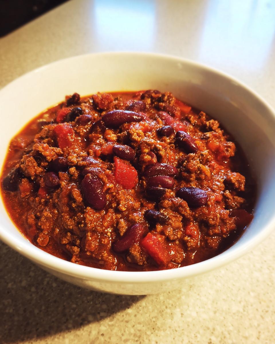 Close-up of a white bowl filled with thick, rich Chili Recipe Crockpot, featuring ground meat and kidney beans.