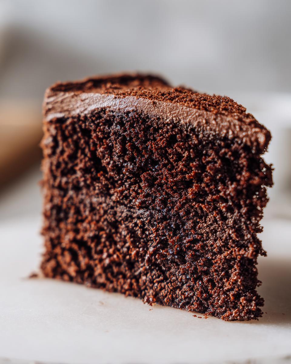 A close-up, macro shot of a moist, dark chocolate slice from a Keto Cakes recipe, topped with chocolate frosting.