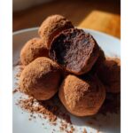 A pile of decadent Christmas Truffles dusted heavily in cocoa powder, one cut open to show the dark center.