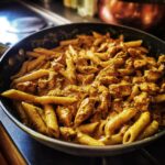 Close-up of creamy Cowboy Butter Chicken Pasta with penne and seasoned chicken chunks in a dark skillet.