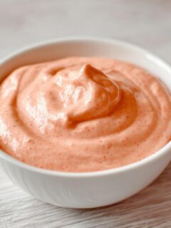 Close-up of a white bowl filled with thick, creamy, pinkish-orange In N Out Sauce.