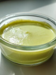 Close-up of a small glass ramekin filled with smooth, light green wasabi sauce.