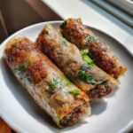 Three golden-brown, crispy Thai Basil Beef Rolls arranged on a white plate, showing visible herbs inside.