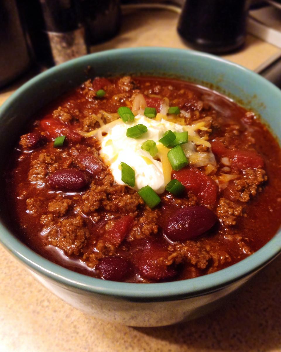 A close-up of a bowl of rich, thick Crockpot Chili topped with sour cream, shredded cheese, and green onions.