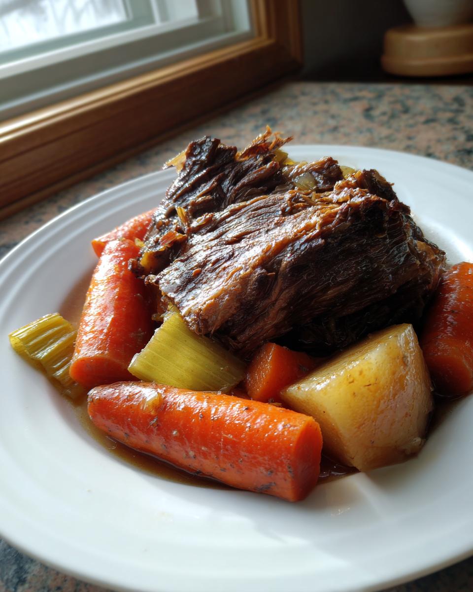 A serving of tender Crockpot Pot Roast with large chunks of cooked carrots and potatoes on a white plate.