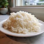 A mound of fluffy, perfectly cooked white Jasmine Rice served on a white plate near a bright window.