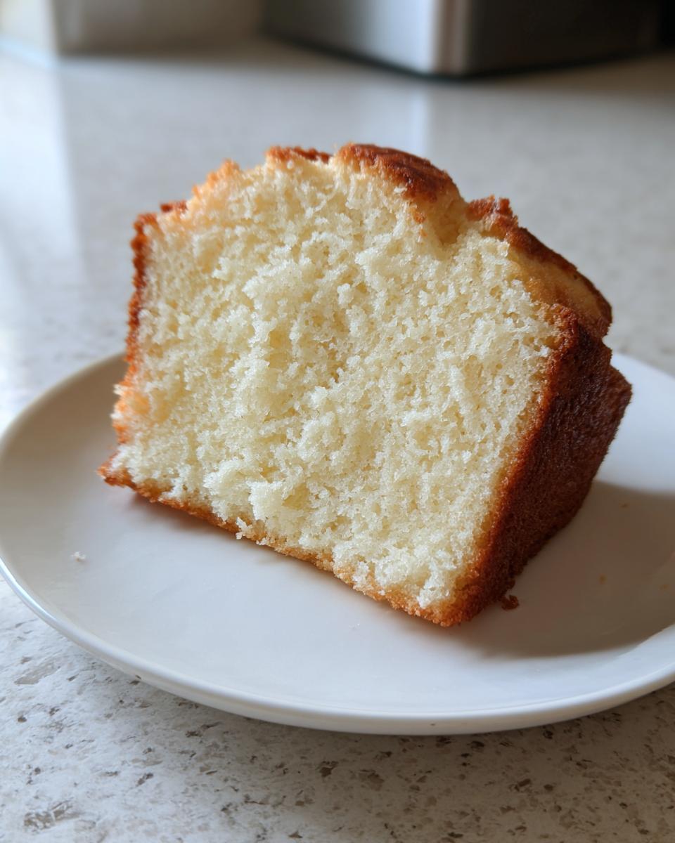 Close-up of a moist, fluffy slice of plain vegan cake on a white plate.