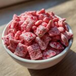 Close-up of a white bowl filled with Fluffy Strawberry Shortcake Puppy Chow coated in pink and red speckles.