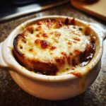 A close-up of bubbling French Onion Soup topped with a thick layer of melted, browned cheese over toasted bread.