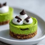 Close-up of a vibrant green Grinch Mini Cheesecake with white frosting eyes and chocolate accents.