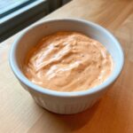 Close-up of creamy, orange-hued In N Out Sauce served in a small white ramekin on a wooden surface.