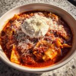 A close-up of a hearty bowl of Lasagna Soup Crockpot, topped with a dollop of ricotta cheese and grated Parmesan.
