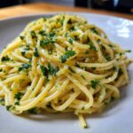 A close-up serving of glistening Lemon Butter Garlic Pasta tossed with finely chopped parsley and garlic.