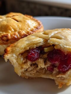 Close-up of two Mini Turkey Cranberry Pies, one cut open revealing shredded turkey and bright red cranberries inside flaky crust.