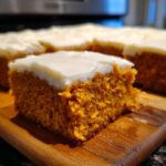 A close-up shot of a thick, moist square of orange Pumpkin Bars topped with smooth white cream cheese frosting.
