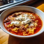 A close-up of a bowl of rich, red One Pot Lasagna Soup topped with dollops of ricotta cheese and grated Parmesan.