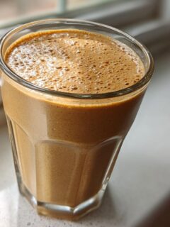 A close-up of a thick, brown PB2 Recipes smoothie with a frothy top, sitting near a window.