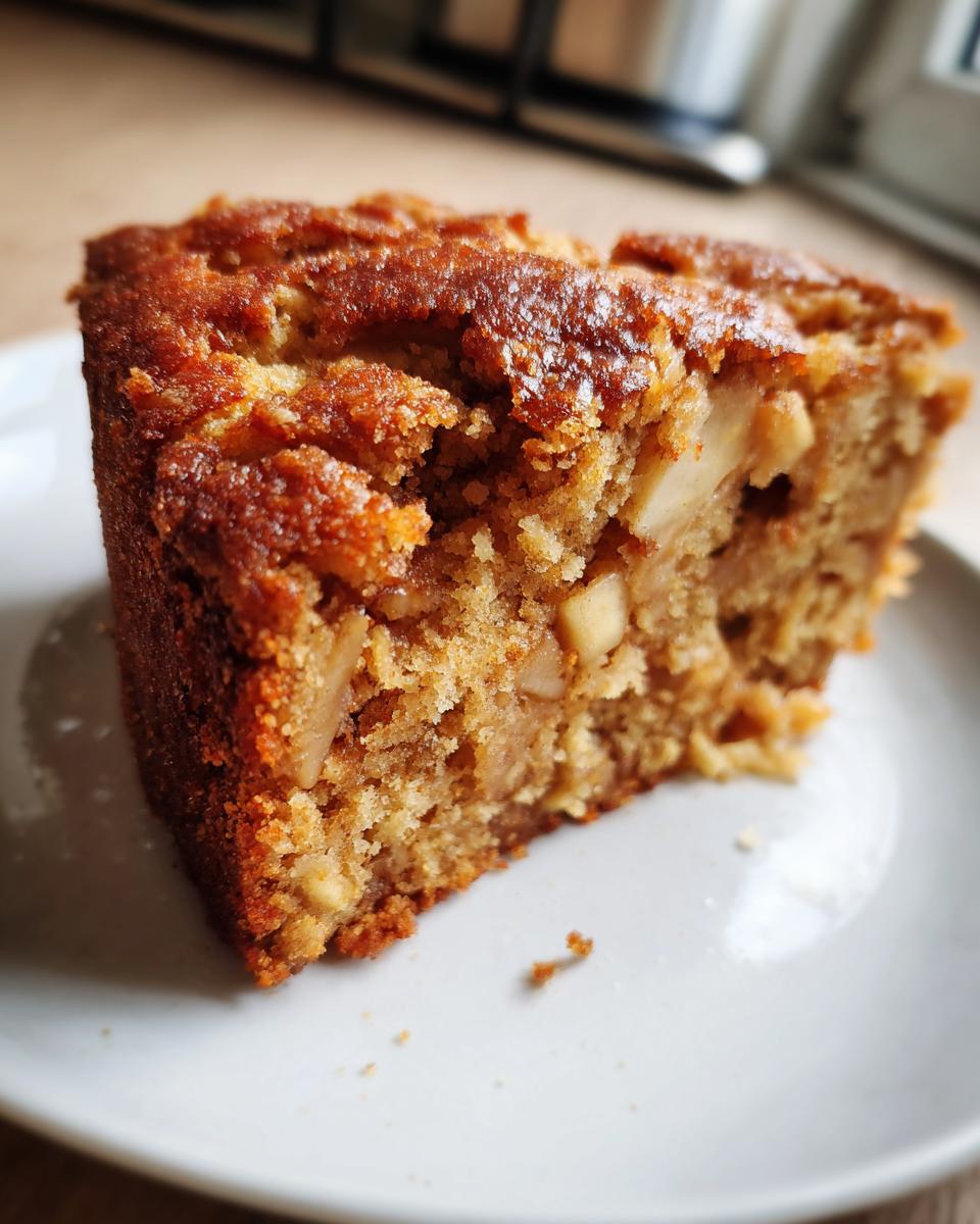 Close-up of a moist, golden-brown slice of apple cake recipe showing chunks of baked apple inside.