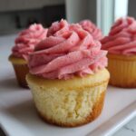 Close-up of a vanilla cupcake topped with vibrant pink raspberry frosting, part of a batch of Raspberry Lemon Cupcakes.