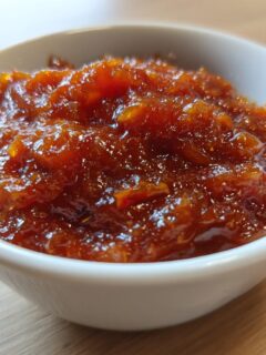 A close-up of thick, dark orange, glistening chutney recipes condiment served in a small white bowl.
