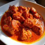 Close-up of tender pieces of chicken coated in a vibrant, creamy orange sauce, ready to eat Butter Chicken.