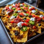 A close-up of fully loaded Sheet Pan Nachos covered in melted cheese, ground beef, salsa, sour cream, and jalape&ntilde;os.