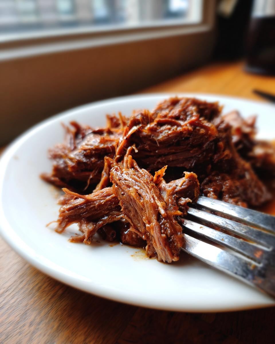 Close-up of tender, shredded Mississippi Pot Roast being lifted by a fork on a white plate.