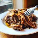 A fork pulling apart incredibly tender, shredded Mississippi Pot Roast served on a white plate with rich juices.