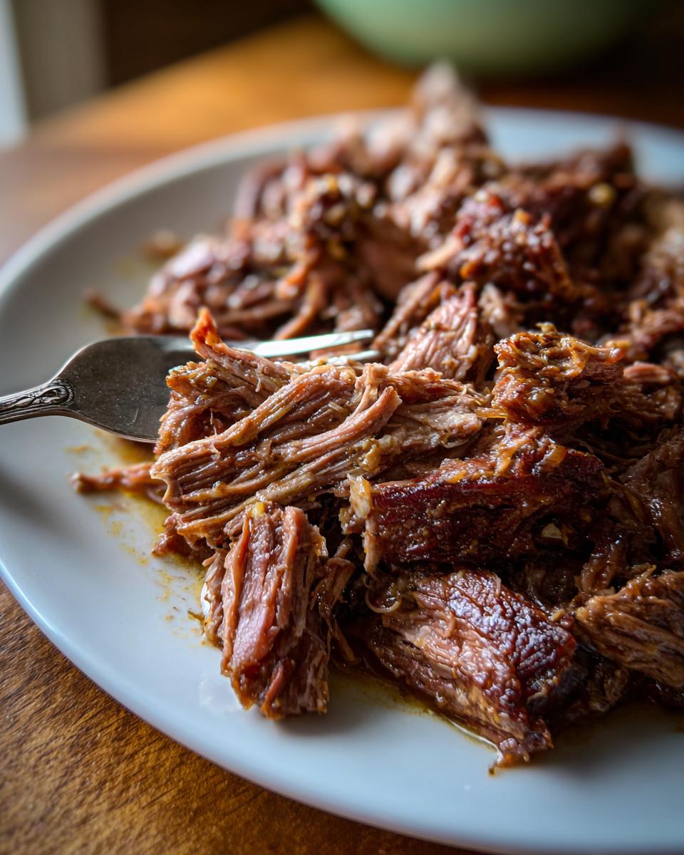 Close-up of tender, shredded Mississippi Pot Roast served on a white plate with a fork.