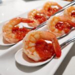 Close-up of chilled shrimp topped with cocktail sauce served on individual white appetizer spoons, perfect for wedding appetizers.