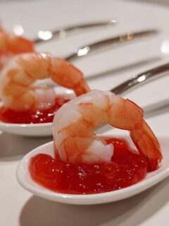 Close-up of elegant shrimp cocktail served on white ceramic spoons as one of the stunning wedding appetizers.