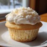 A single, moist vanilla Sugar Free Cupcakes topped with thick white frosting and shredded coconut flakes.