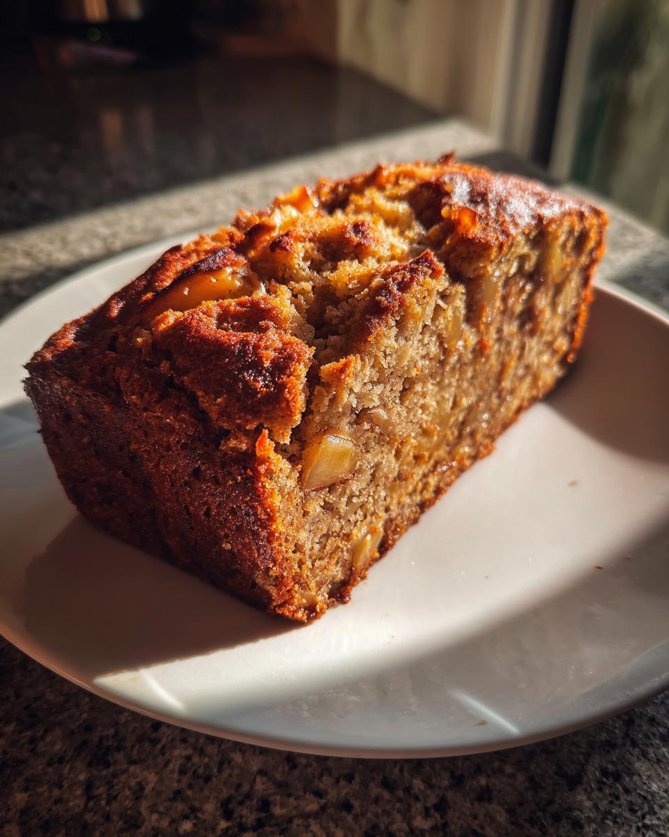 A thick slice of moist Apple Bread with visible apple chunks, sitting on a white plate.