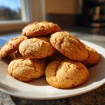 A stack of golden brown, soft Apple Cookies piled high on a white plate, backlit by sunlight.