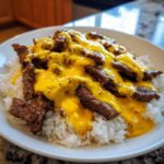 A white bowl filled with white rice topped with sliced steak and smothered in bright yellow queso sauce for a Steak Queso Rice Dinner.