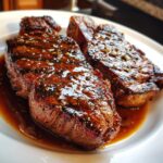 Two perfectly grilled steaks generously coated in a glossy Steak With Bourbon Garlic Sauce on a white plate.