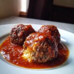Close-up of three juicy Stuffed Meatballs In Gravy served on a white plate, showing melted cheese oozing out.