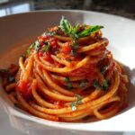 Close-up of a beautiful mound of Tomato Basil Pasta coated in rich red sauce and topped with fresh basil leaves.