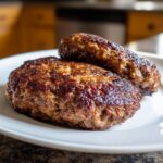 Close-up of two perfectly seared, juicy Crack Burgers resting on a white plate.