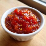 Close-up of a small white bowl filled with vibrant, chunky red chutney recipes, showing visible seeds and glossy texture.