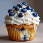 A close-up of a White Chocolate Blueberry Cupcakes with creamy frosting and fresh blueberries on top.