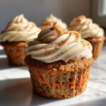 A close-up of one perfectly frosted Carrot Cake Cupcakes, sprinkled with cinnamon, sitting on a marble surface.