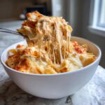 A fork lifts a serving of cheesy, saucy Chicken Parmesan Casserole, showing long cheese pulls.