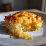 A close-up of a serving of Cheesy Potato Casserole showing melted, stringy cheddar cheese on top of shredded potatoes.
