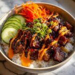 Close-up of Chicken Bulgogi Bowls With Gochujang Spicy Mayo served over rice with cucumbers and carrots.