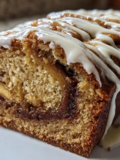 A close-up of a loaf of Cinnamon Roll Banana Bread, sliced to show the swirl and topped with white icing drizzle.